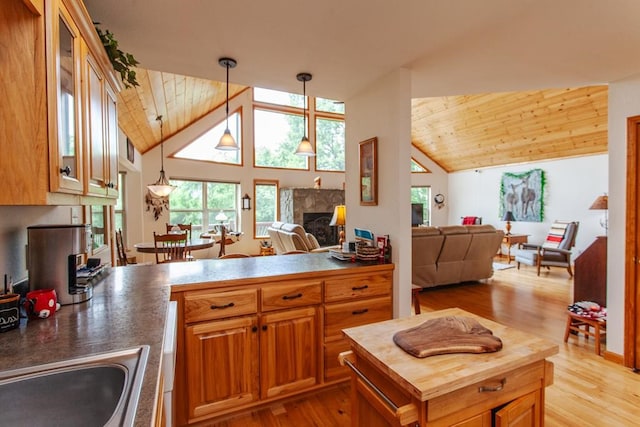 kitchen featuring lofted ceiling, hanging light fixtures, light hardwood / wood-style flooring, wood ceiling, and a tiled fireplace