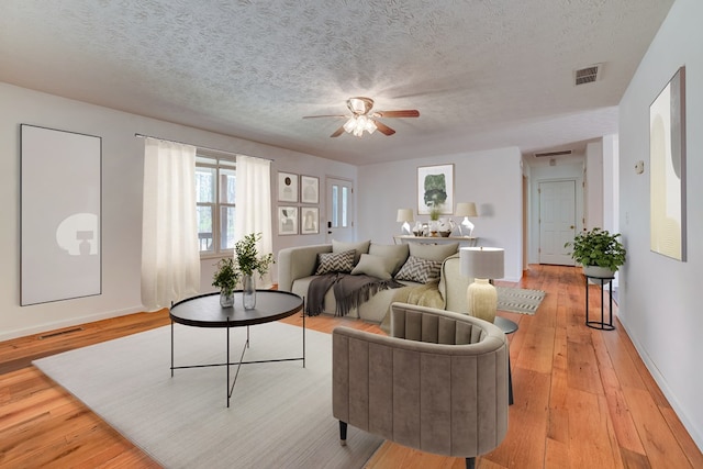 living room with a textured ceiling, light hardwood / wood-style floors, and ceiling fan