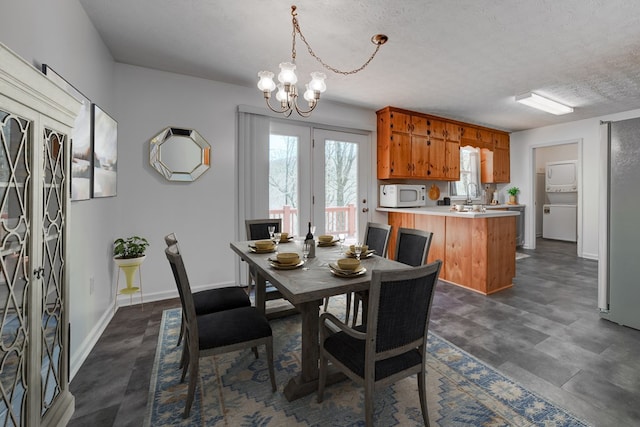 dining space with stacked washer and clothes dryer, french doors, a textured ceiling, and a notable chandelier