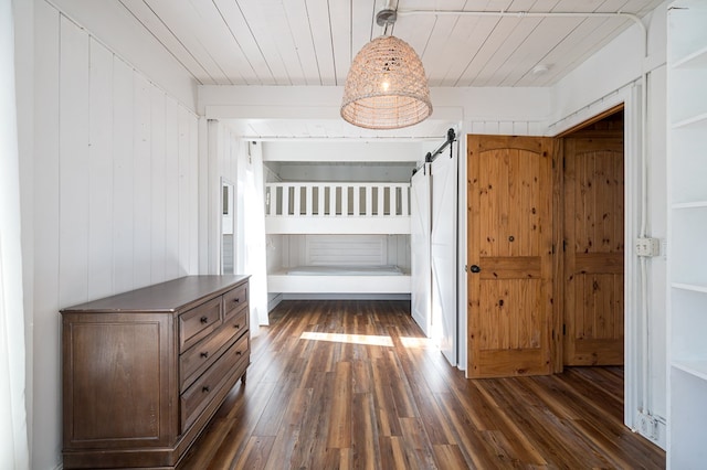 unfurnished bedroom with a barn door, wooden walls, dark hardwood / wood-style flooring, and wood ceiling