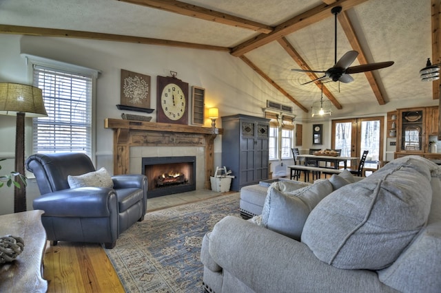 living area with ceiling fan, a fireplace, vaulted ceiling with beams, and wood finished floors