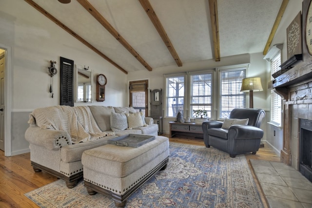 living room with a textured ceiling, wood finished floors, beamed ceiling, and a tile fireplace