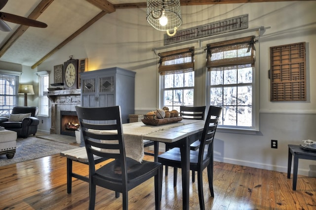 dining space with wood-type flooring, baseboards, beam ceiling, and a tile fireplace