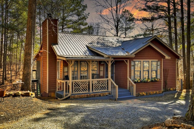 chalet / cabin with covered porch, a chimney, metal roof, and a standing seam roof