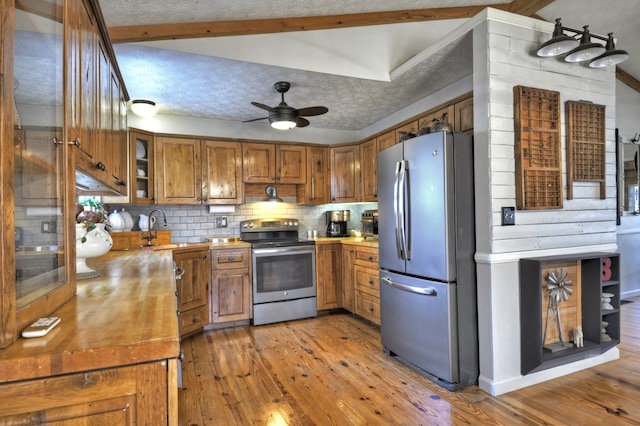 kitchen featuring a textured ceiling, light wood-style flooring, stainless steel appliances, brown cabinets, and tasteful backsplash