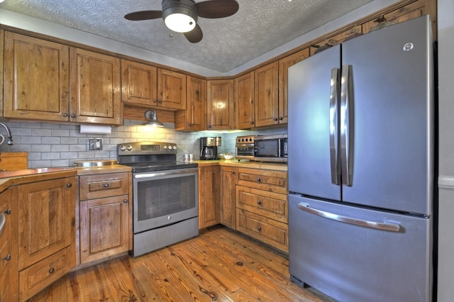 kitchen featuring brown cabinetry, appliances with stainless steel finishes, wood finished floors, a textured ceiling, and backsplash