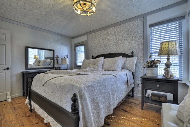 bedroom featuring a textured ceiling, wood finished floors, and wallpapered walls