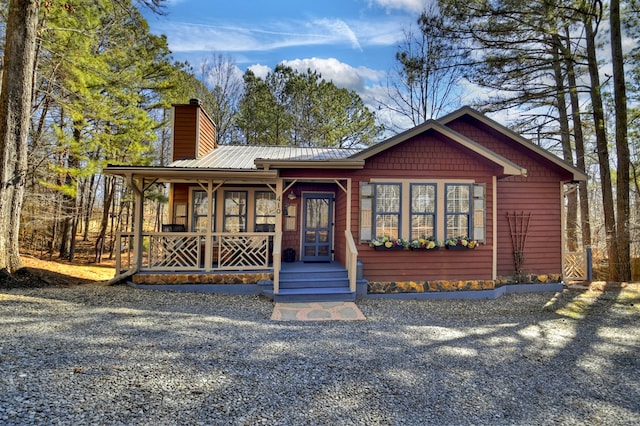 rustic home featuring covered porch, metal roof, and a chimney