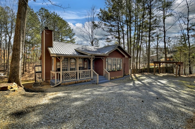 chalet / cabin featuring driveway, a chimney, metal roof, covered porch, and a standing seam roof