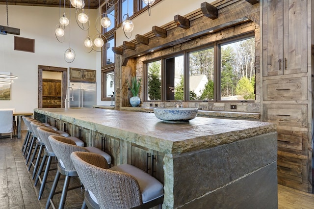 kitchen featuring a kitchen breakfast bar, built in fridge, high vaulted ceiling, decorative light fixtures, and hardwood / wood-style flooring