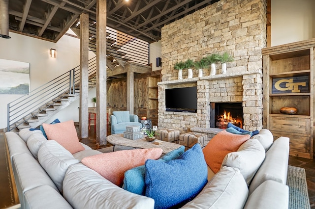 living room featuring a stone fireplace, built in shelves, a towering ceiling, and wood-type flooring