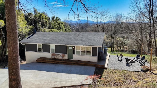 single story home with an outdoor fire pit, a shingled roof, a patio, a deck with mountain view, and brick siding