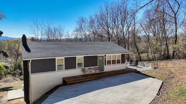 ranch-style home featuring roof with shingles, brick siding, a chimney, and a patio area