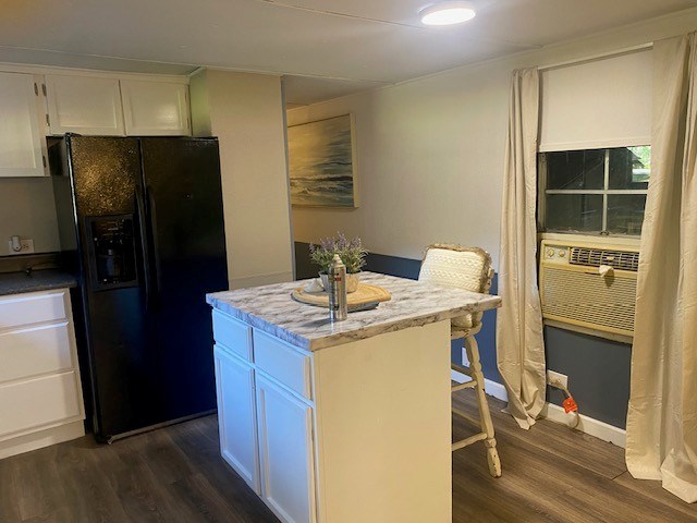 kitchen with a kitchen island, dark wood-type flooring, black refrigerator with ice dispenser, a kitchen bar, and white cabinetry