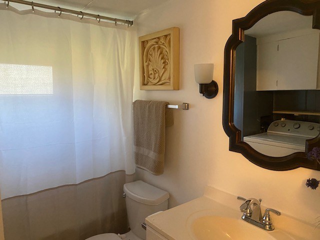 bathroom with toilet, walk in shower, vanity, and washer / dryer