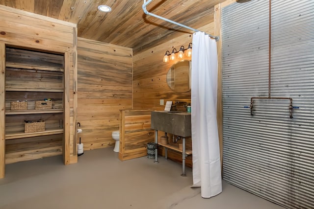 interior space featuring wooden ceiling, toilet, wooden walls, a sink, and finished concrete floors