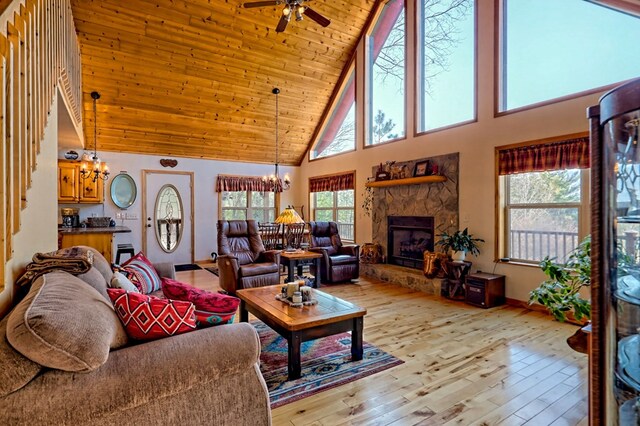 living area with wood ceiling, light wood-type flooring, a stone fireplace, ceiling fan with notable chandelier, and high vaulted ceiling