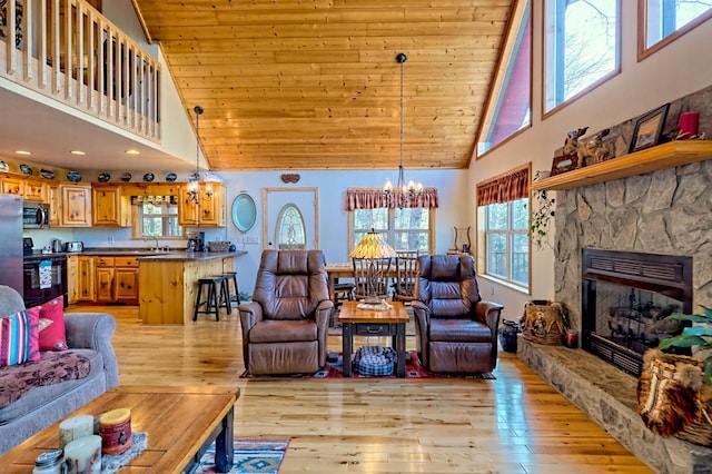 living room featuring a stone fireplace, an inviting chandelier, light wood-type flooring, and wooden ceiling