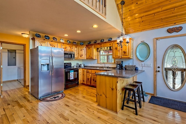 kitchen with a peninsula, stainless steel appliances, a kitchen bar, dark countertops, and light wood-type flooring