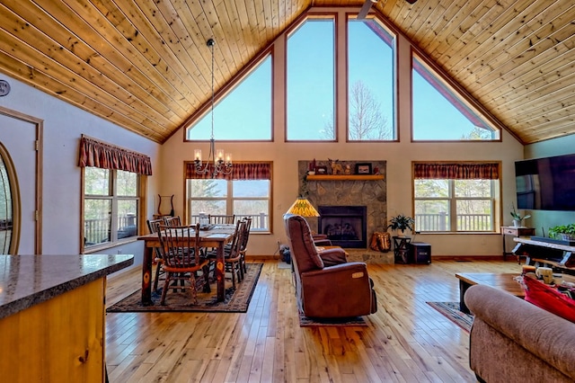 living room featuring a stone fireplace, wood ceiling, light wood-type flooring, and a chandelier