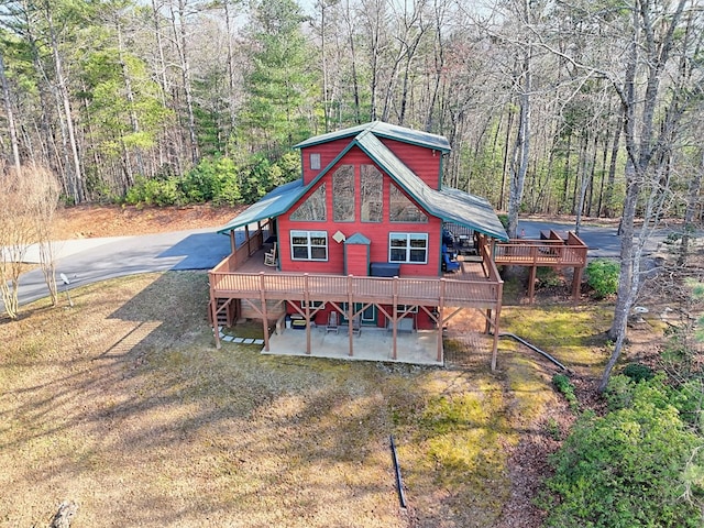 exterior space featuring a wooden deck, a patio, a wooded view, and driveway