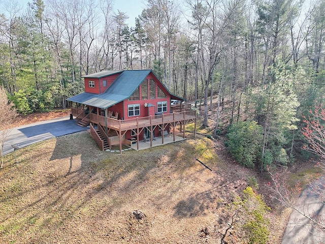 exterior space with dirt driveway, stairs, a view of trees, a deck, and a patio