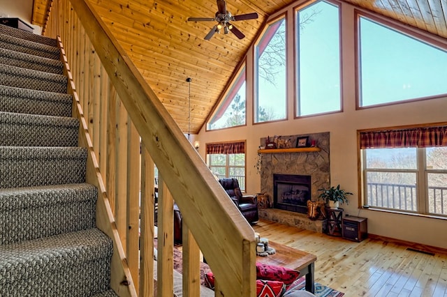 stairs featuring a stone fireplace, wood ceiling, hardwood / wood-style floors, and ceiling fan