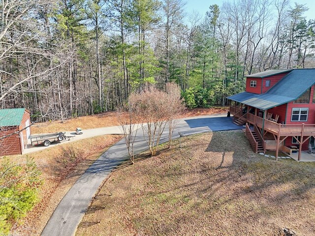 view of yard featuring stairs, a wooded view, and driveway