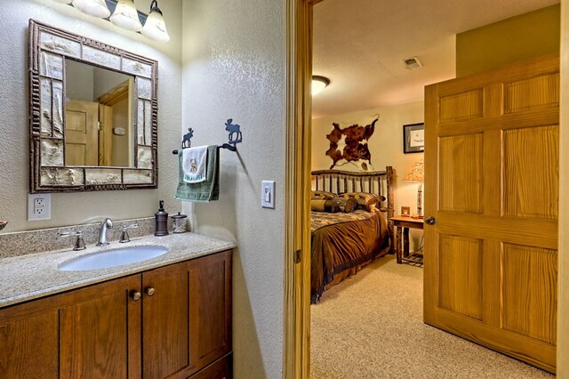 bathroom with vanity, a textured wall, visible vents, and connected bathroom