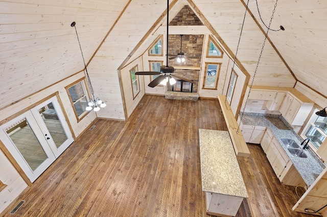 unfurnished living room with ceiling fan, vaulted ceiling, dark wood-type flooring, sink, and wood walls