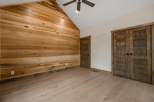 spare room featuring light hardwood / wood-style flooring, high vaulted ceiling, ceiling fan, and wood walls