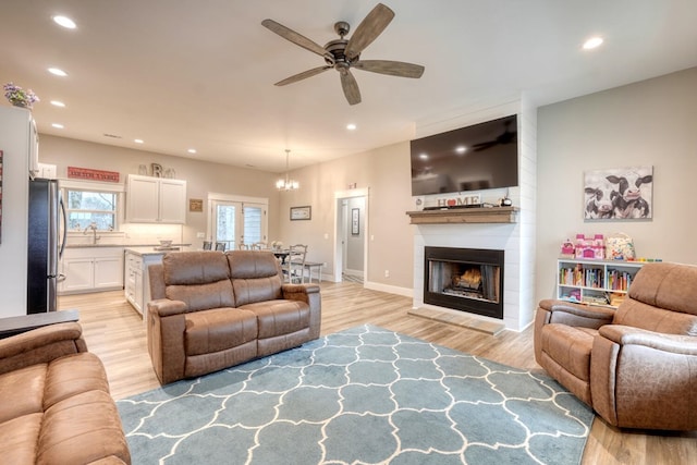 living room featuring a large fireplace, ceiling fan with notable chandelier, and light wood-type flooring