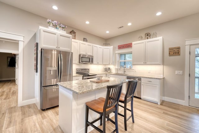 kitchen featuring a breakfast bar, light stone counters, appliances with stainless steel finishes, a kitchen island, and white cabinets