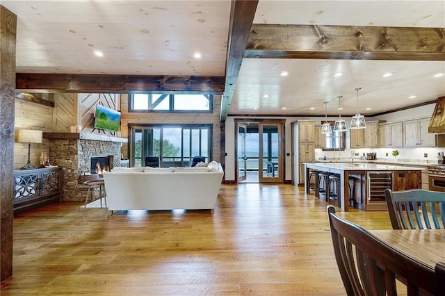 living room with wine cooler, a fireplace, beamed ceiling, and light wood finished floors