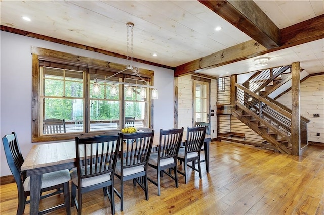 dining area featuring light wood-type flooring, wooden walls, stairway, and beamed ceiling