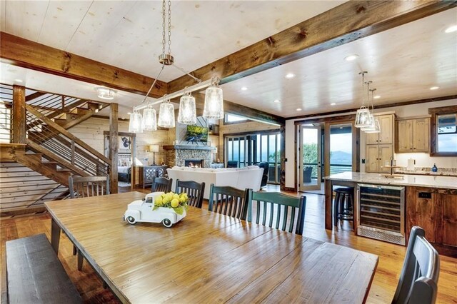 dining space with beverage cooler, stairway, light wood-style floors, a fireplace, and beam ceiling