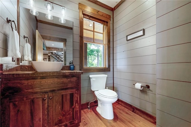 bathroom with wood walls, vanity, toilet, and wood finished floors