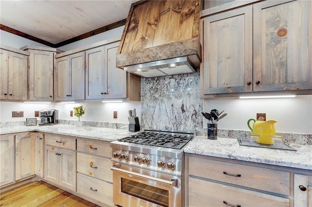 kitchen with light stone counters, tasteful backsplash, custom range hood, light wood-style floors, and high end range