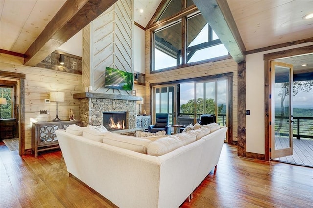 living room with a stone fireplace, wood finished floors, beam ceiling, and wooden walls