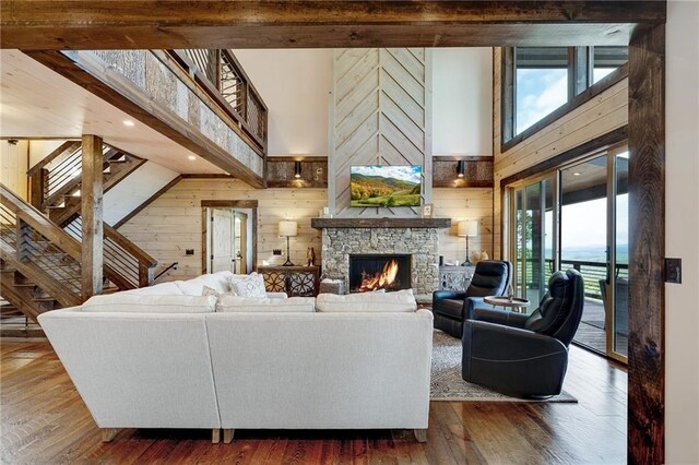 living area featuring dark wood-type flooring, a stone fireplace, wooden walls, and stairs