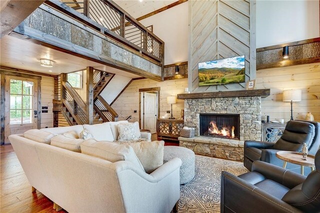 living area with a stone fireplace, a high ceiling, wood finished floors, and wooden walls