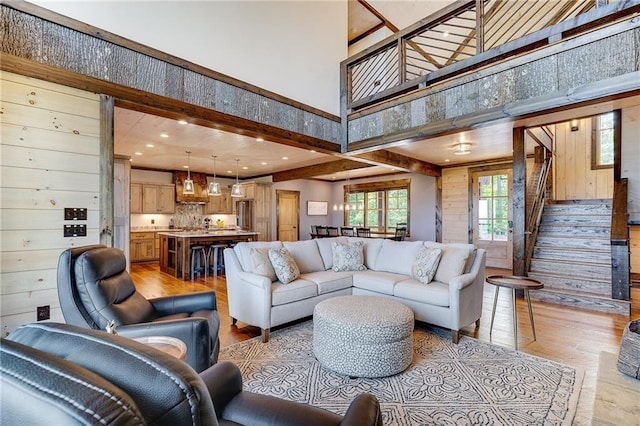 living room featuring recessed lighting, wood walls, a towering ceiling, stairs, and light wood-type flooring