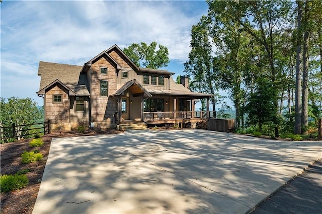 view of front of house with a porch, fence, stone siding, board and batten siding, and a chimney