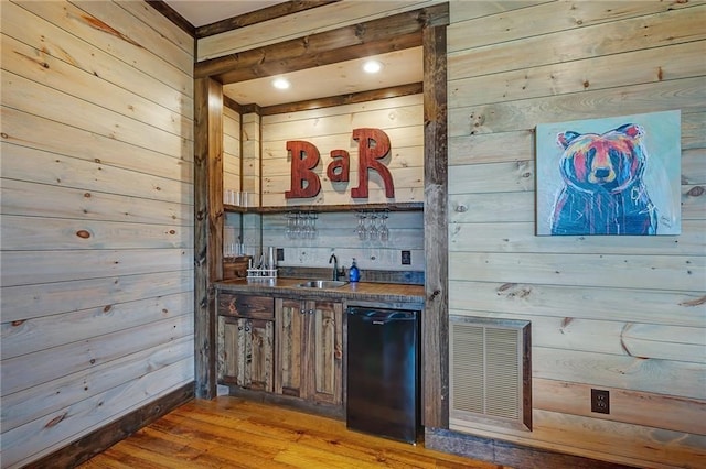 bar with light wood-type flooring, indoor wet bar, visible vents, and wooden walls