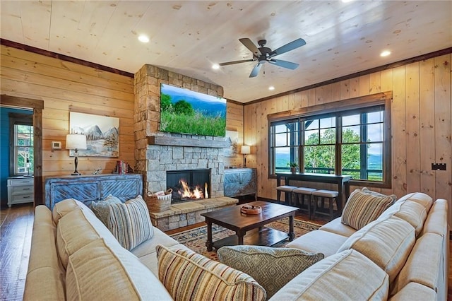 living room featuring ceiling fan, a stone fireplace, recessed lighting, wooden walls, and wood finished floors