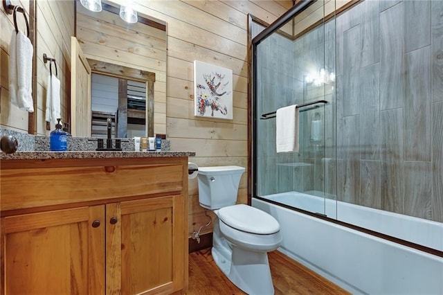 bathroom with wooden walls, toilet, enclosed tub / shower combo, wood finished floors, and vanity