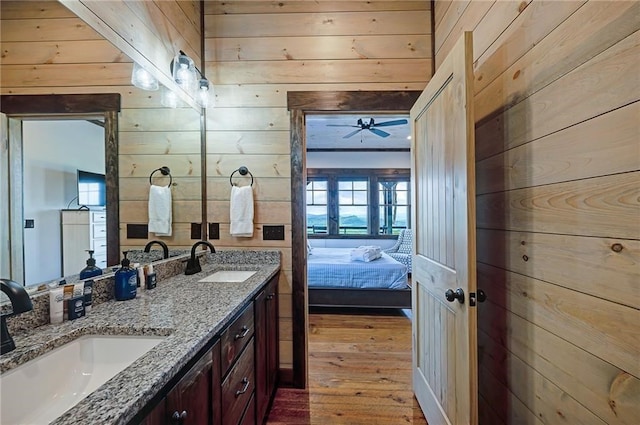 ensuite bathroom featuring double vanity, wood walls, ensuite bath, and a sink