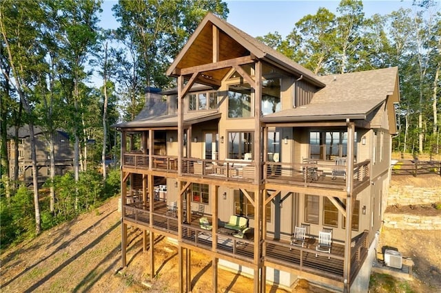 back of house featuring roof with shingles, a chimney, a balcony, and central air condition unit