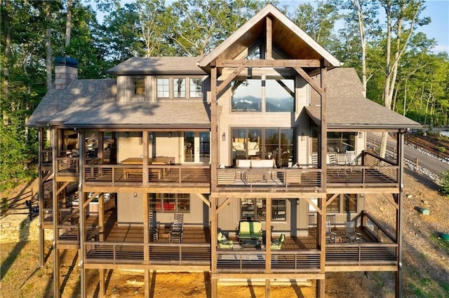 rear view of house featuring a deck, a shingled roof, a chimney, and outdoor lounge area