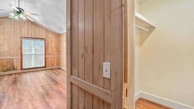 interior space featuring baseboards, wood finished floors, vaulted ceiling, a textured ceiling, and wood walls